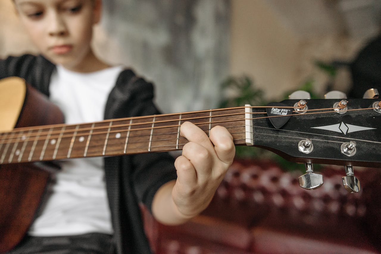 A child playing an acoustic guitar indoors with focus on fretboard and fingers.