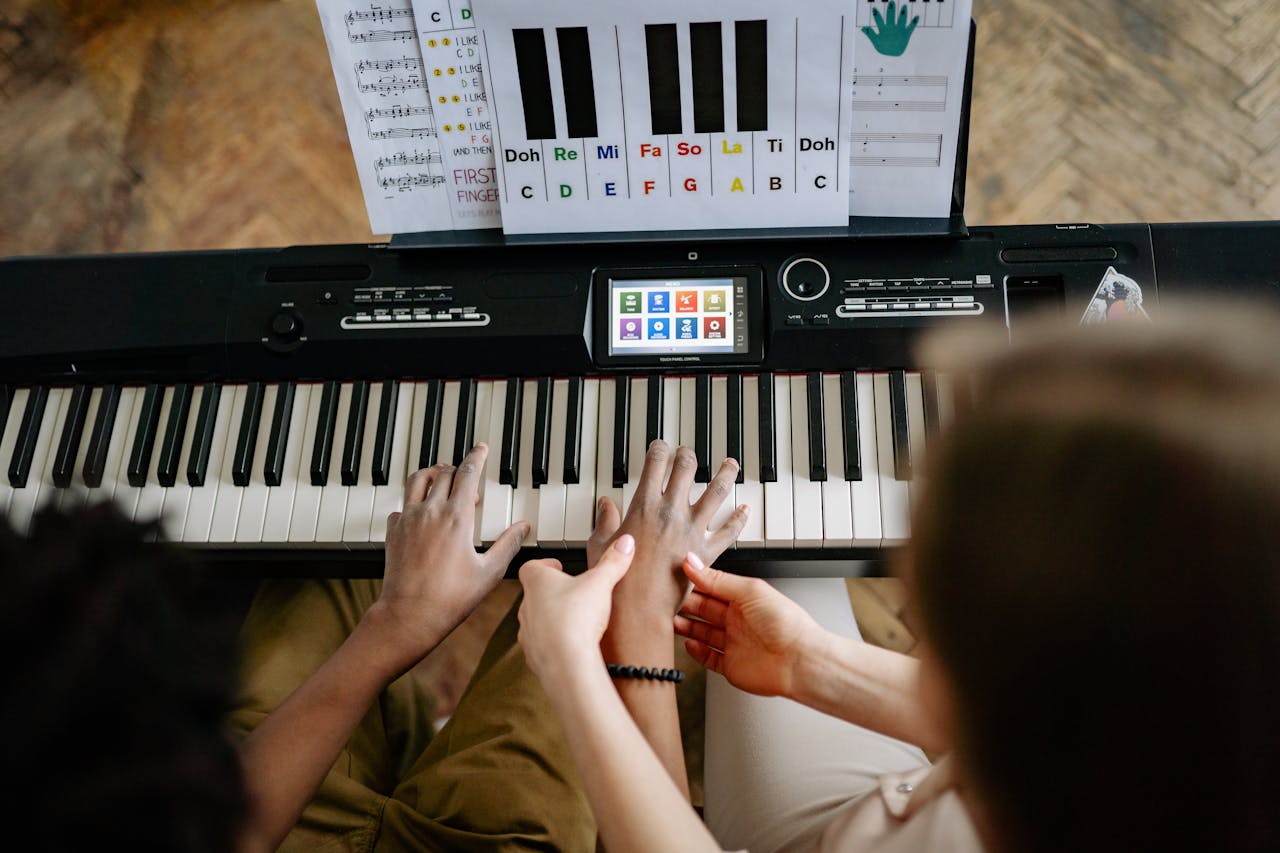 A woman guides a students hands on a keyboard piano, emphasizing musical instruction.