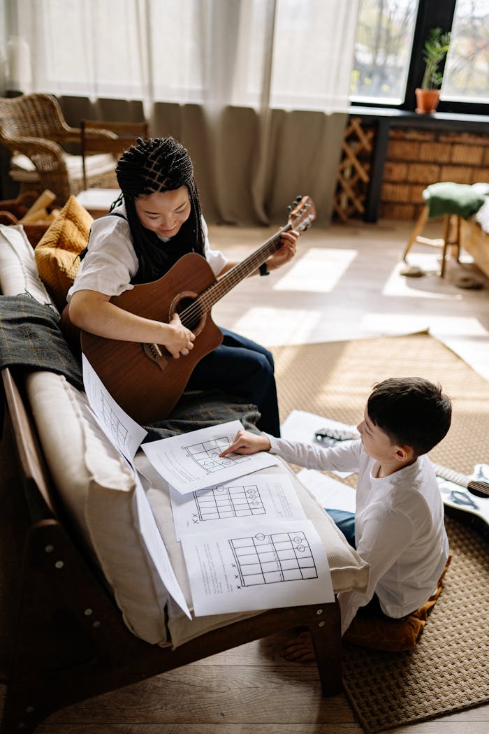 A young boy and a woman engage in a music lesson, focusing on guitar, at home.